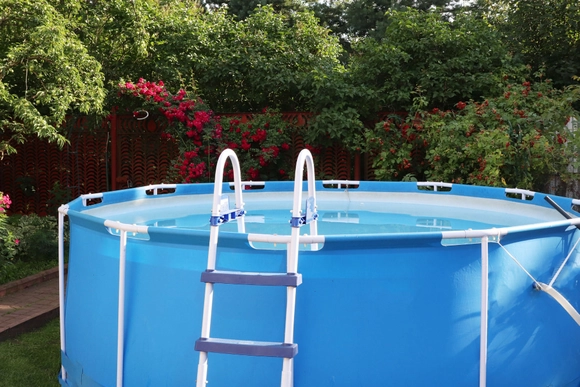 Ein blauer Aufstellpool mit Leiter steht in einem Garten.
